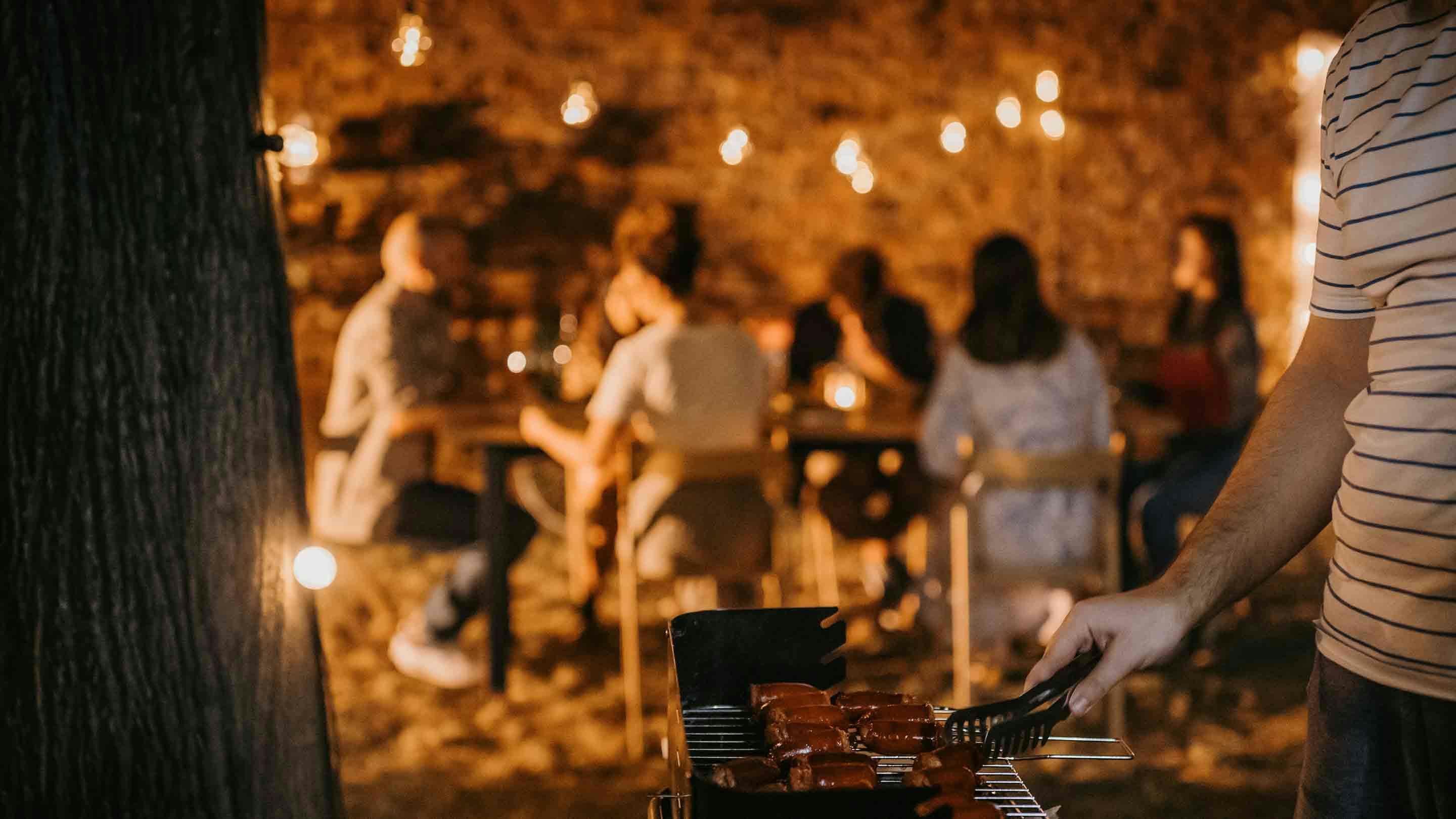 Prijatelji uživaju u GRILL večeri s dekorativnim lampicama